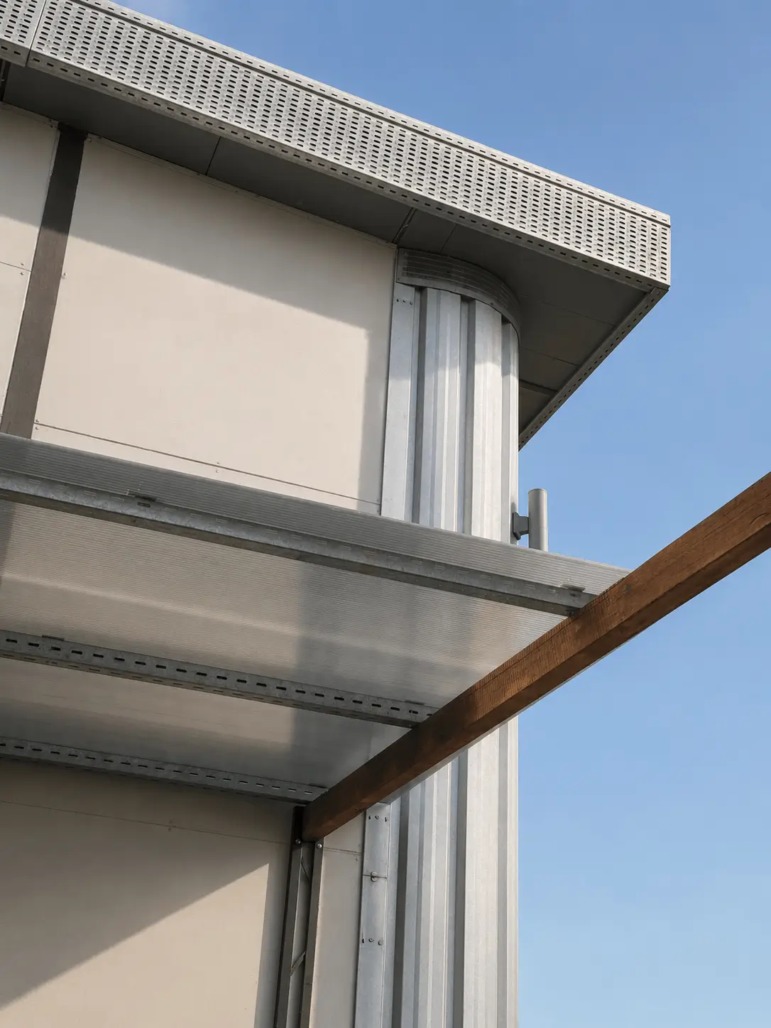Metal building corner with a clear roof panel and wooden beam against a blue sky.