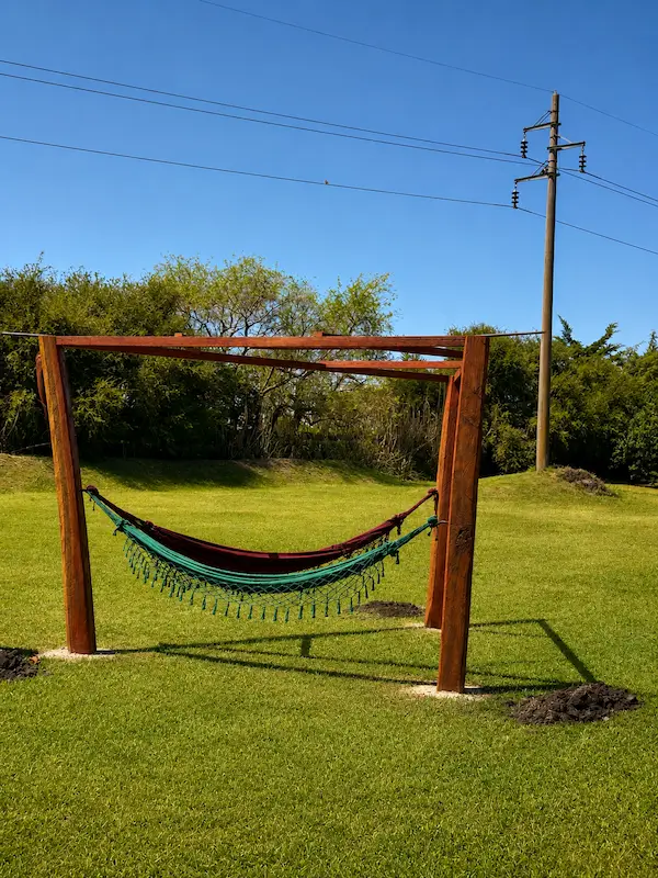 Green and burgundy hammock hanging on a wooden frame on bright green grass under a blue sky.