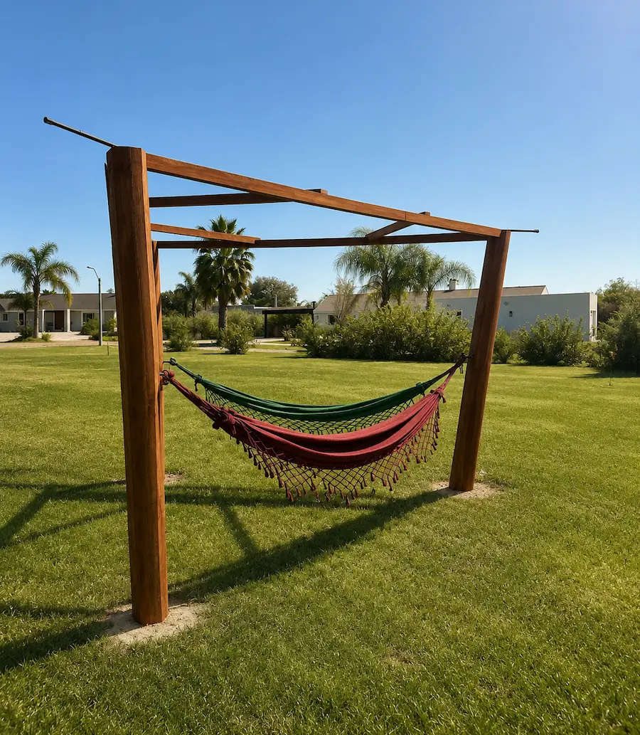 Two hammocks, one green and one red, hanging on a wooden frame on a green lawn with trees and houses behind.